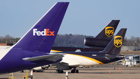 Vista cercana de las colas de aviones de carga de FedEx y UPS estacionados uno al lado del otro en la pista del aeropuerto.
