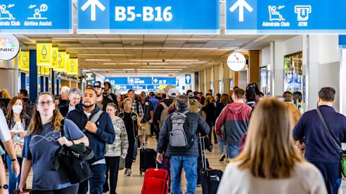 Crowded airport concourse with travelers walking beneath overhead signs for gates B5 to B16.