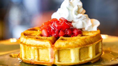 Waffle cubierto con fresas y crema batida en un plato.