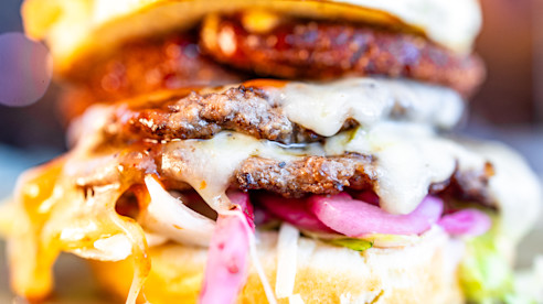 Primer plano de una hamburguesa con queso derretido, cebolla y salsa.