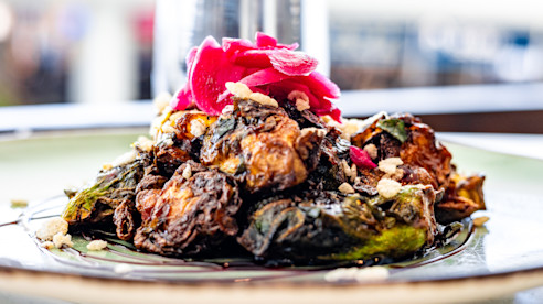 Plato con verduras asadas y carne, cubierto con cebollas encurtidas y guarnición.