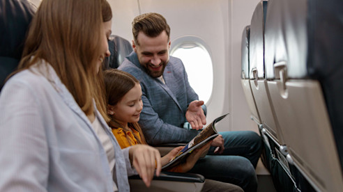 Una familia se sienta junta en un avión y sonríe mientras miran una revista durante el vuelo.