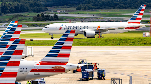 An airport scene featuring multiple American Airlines planes parked at the gate, with one aircraft taxiing on the runway, highlighting the airport's busy operations.