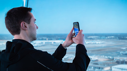 Un hombre toma una foto del campo de aviación del aeropuerto a través de una gran ventana con su teléfono móvil. 