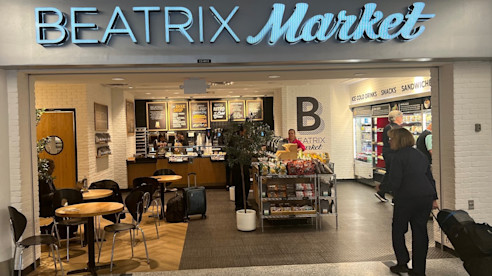 Beatrix Market restaurant at the airport with seating, food displays, and travelers nearby.