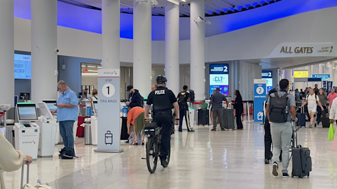 A police officer on a bicycle patrols the airport ticketing area as travelers check in and walk toward security.