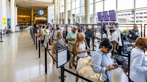 Pasajeros hacen fila en el control de seguridad del aeropuerto, esperando con sus identificaciones y pases de abordar.