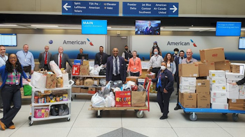 Empleados del aeropuerto posan detrás de carritos llenos de cajas y bolsas con donaciones en el área de boletos de American Airlines.