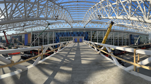 Interior view of a steel truss canopy under construction with cranes and equipment at an airport terminal.