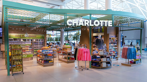 Charlotte airport shop with snacks, drinks, and apparel displays under a bright green storefront sign.