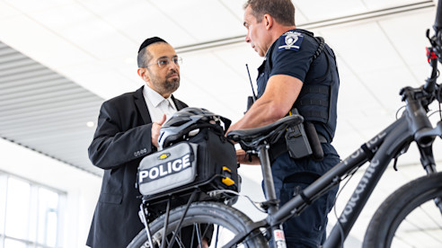 A police officer talking with a man beside a police bicycle inside an airport terminal.