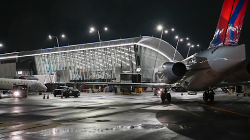 Illuminated airport concourse at night with Delta aircraft parked at gates, ground vehicles, and a modern glass terminal.
