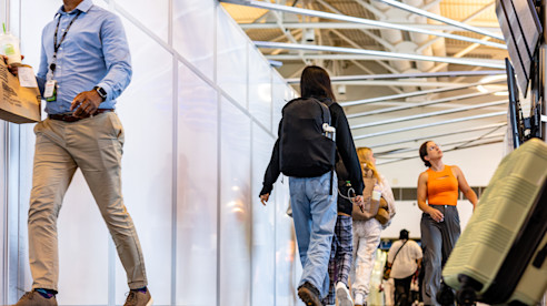 Travelers walking through an airport hallway with construction barriers on one side and rolling luggage nearb