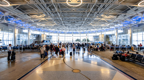  Crowded airport terminal with travelers walking and sitting near boarding gates under a modern, circular ceiling design.