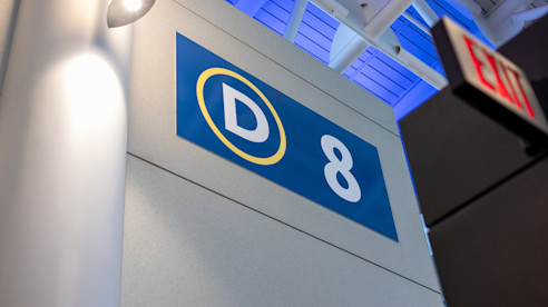 Close-up of gate sign D8 in an airport with an EXIT sign visible nearby.