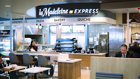 La Madeleine Express restaurant inside the airport with seating, menu boards, and travelers dining.