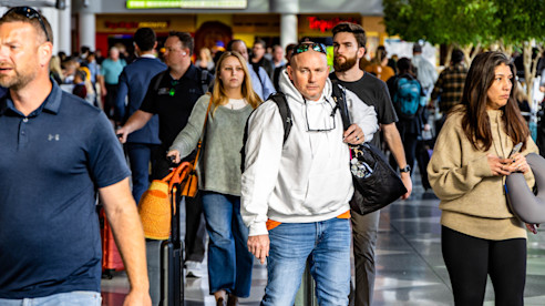 Crowded airport terminal with travelers walking through the concourse carrying bags and personal items.