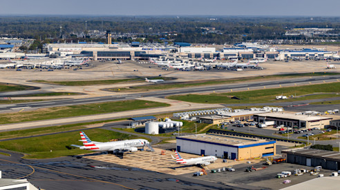 Aerial view of an airport with terminals, runways, service buildings, and parked aircraft across the airfield.