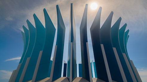 A striking modern sculpture with tall, curved blue panels reaches toward the sky, illuminated by the sun.