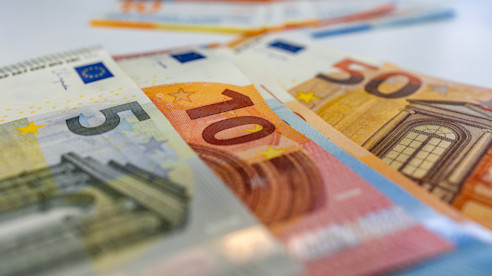 Primer plano de billetes de euro de 5, 10 y 50 esparcidos sobre una superficie blanca.