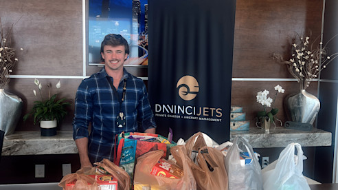 Hombre está detrás de un mostrador con varias bolsas de donaciones de alimentos en un vestíbulo.
