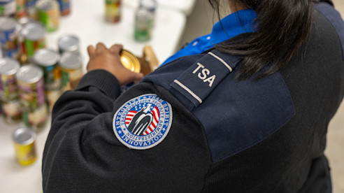Empleada de TSA organiza donaciones de alimentos enlatados en una mesa durante un evento comunitario.