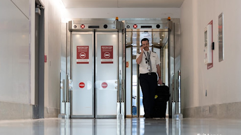 Airline crew member with luggage exits through automated security doors marked with red “Do Not Enter” signs.