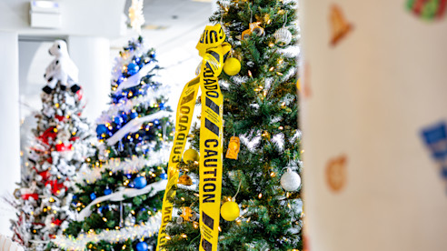 Árboles navideños decorados en interior, uno envuelto con cinta amarilla de precaución.