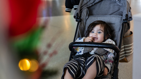 Niño pequeño sentado en un cochecito en interior, con decoraciones navideñas desenfocadas al frente.
