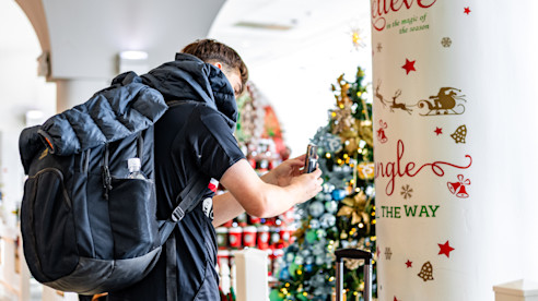 Viajero con mochila toma una foto de una exhibición navideña junto a una columna decorada.