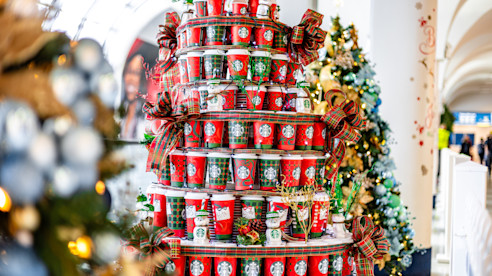 Árbol decorativo navideño hecho de vasos de café rojos y verdes, adornado con moños y decoraciones.