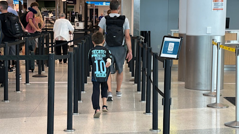 Father and son walking through airport security line, with the child wearing a soccer jersey.
