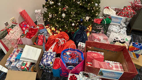 Regalos envueltos y bolsas de donaciones están colocados debajo de un árbol de Navidad decorado en interior.