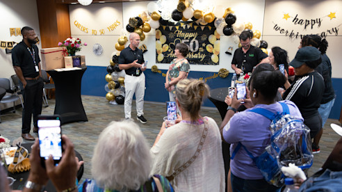 Janice Futrell stands in front of a crowd during her 50-year anniversary celebration, with decorations and speeches.