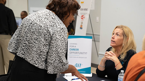 Airport staff member speaks with a visitor at a table promoting career opportunities inside the terminal.