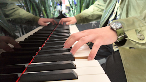 Close-up of hands playing piano keys inside an airport terminal.