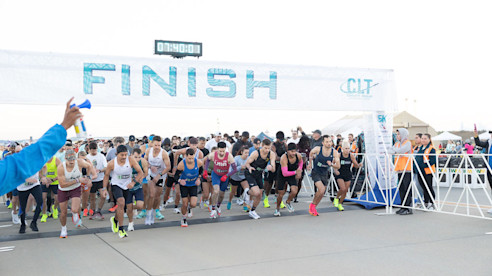 Runners start a race beneath a large FINISH banner during a public runway event at the airport.