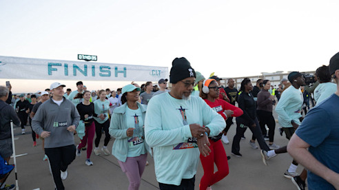 Runners move past a FINISH banner during an airport runway race, with participants checking watches and jogging together.