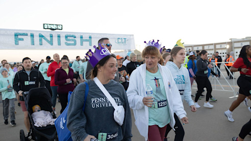 Participants walk and jog past a FINISH banner during an airport runway race, including families and strollers.