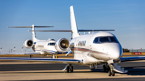 Two sleek white private jets parked on an airport tarmac under a clear blue sky.