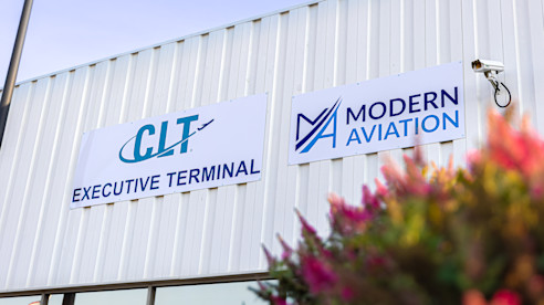 Building signs for CLT Executive Terminal and Modern Aviation, with flowers in the foreground.