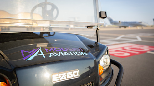 Modern Aviation-branded EZGO cart parked on an airport tarmac with a jet in the background.
