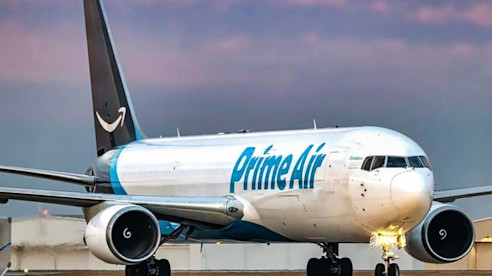 Avión de carga Prime Air en la pista, con motores encendidos y cielo vespertino de fondo.