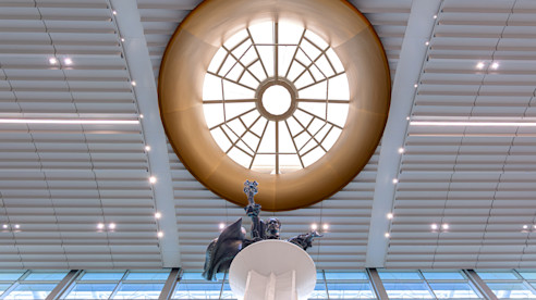 Cúpula con diseño geométrico iluminada por luz natural sobre una estatua que sostiene objetos.