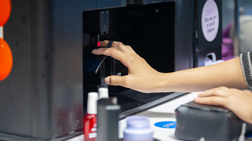 Person receiving a robotic manicure at an airport kiosk, with a hand placed inside the automated nail painting machine.