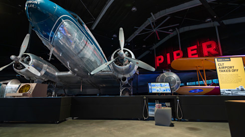 Exhibición de aviones históricos con letrero neón "PIPER" en museo de aviación.