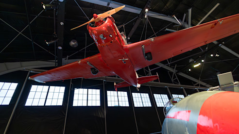 Avión antiguo rojo suspendido del techo del museo en posición de vuelo