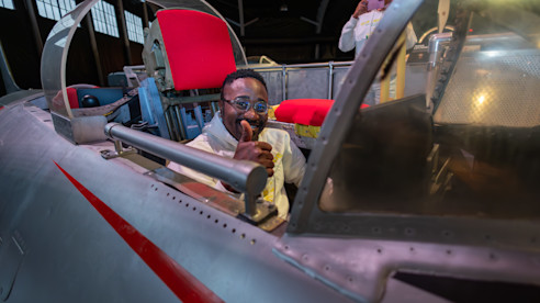 Hombre sonriente haciendo pulgar arriba dentro de la cabina de un avión antiguo.