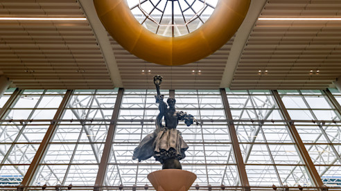 Gran estatua bajo un tragaluz dentro de la terminal del aeropuerto con paredes y techo de vidrio.