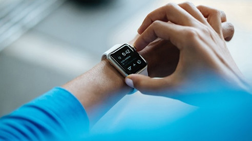 Una persona con camisa azul revisa la hora en un reloj inteligente.